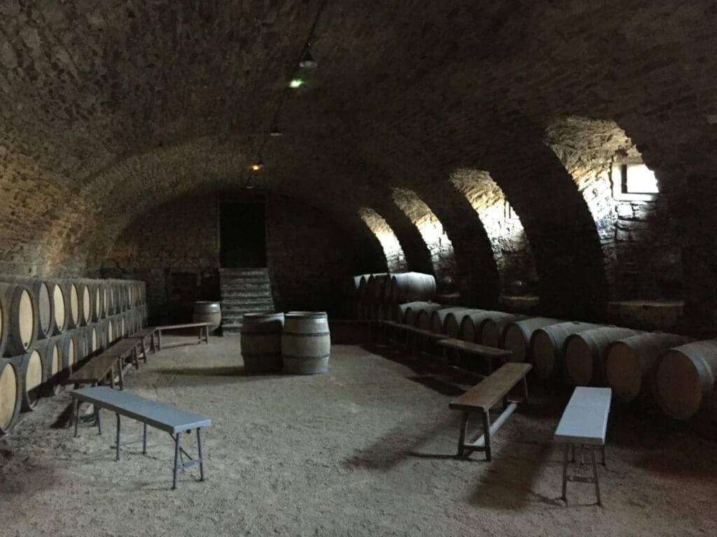 Cave voûtée en pierre avec rangées de fûts de vin pour dégustation.