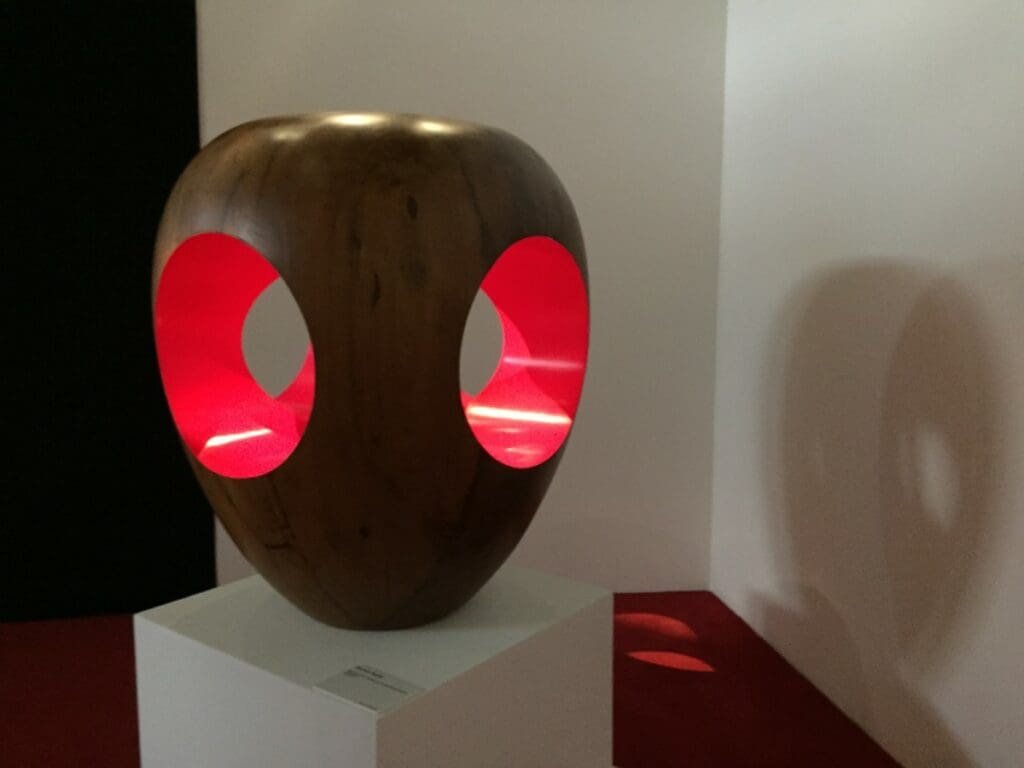 Expo Yom de Saint Phalle -DR Valérie Collet 2019 Sculpture moderne en bois avec ouvertures lumineuses rouges en exposition.
