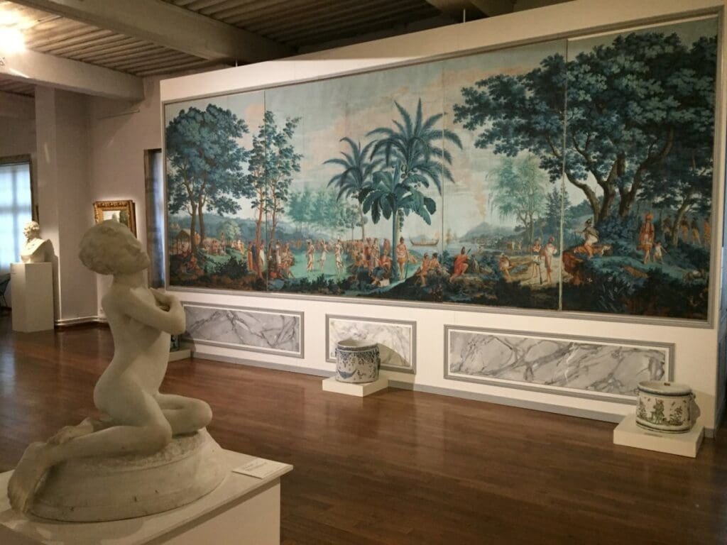 Musée des Ursulines -DR Valérie Collet 2019 Sculpture d'enfant agenouillé devant une fresque panoramique exotique au Musée des Ursulines.