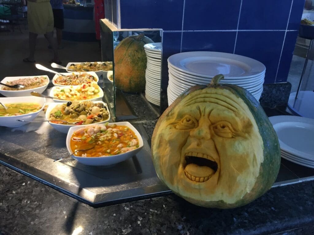 Citrouille sculptée d'un visage expressif à un buffet de plats cubains.