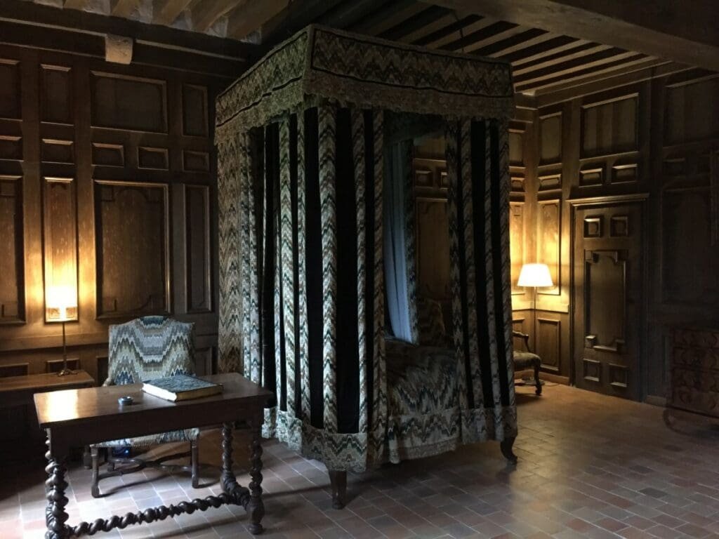 Chambre du château de Talcy avec lit à baldaquin d'époque et boiseries sombres.