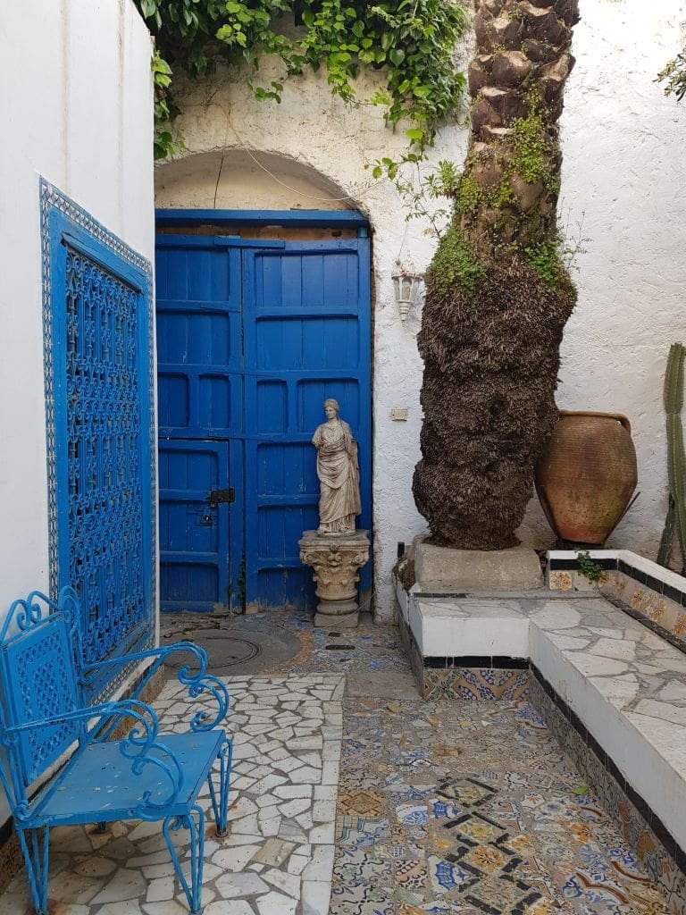 Cour intérieure de Sidi Bou Saïd avec porte bleue, banc en fer et statue.