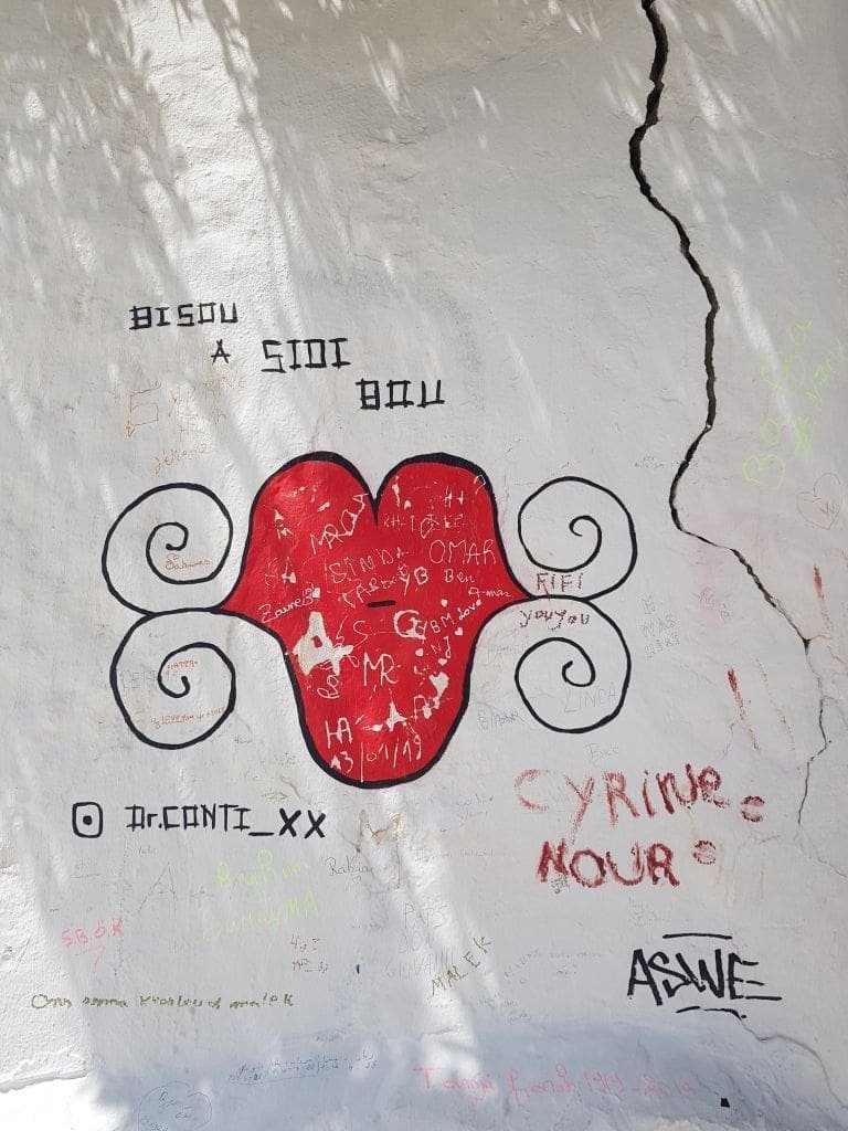 Bambalouni Sidi Bou Saïd - DR Melle Bon Plan 2019 Graffiti "Bisou à Sidi Bou" avec cœur rouge et signatures sur mur blanc à Sidi Bou Saïd.