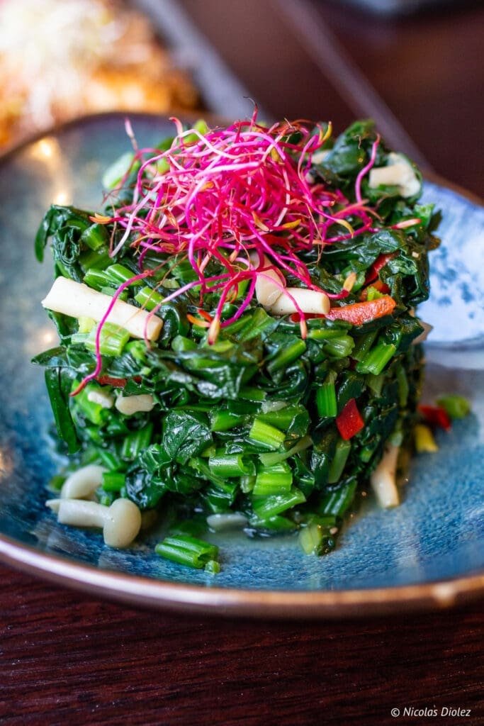 Légumes sautés asiatiques avec pousses de betterave rouge sur assiette bleue.