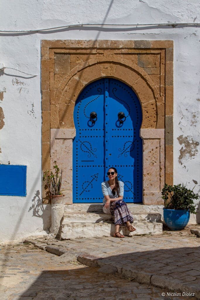 Femme assise devant une porte bleue traditionnelle à Sidi Bou Saïd.
