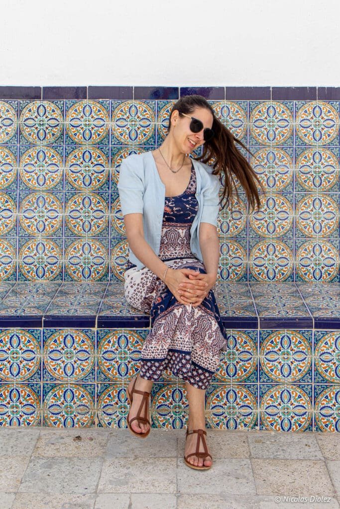 Femme souriante assise sur banc en carreaux colorés à Sidi Bou Saïd.