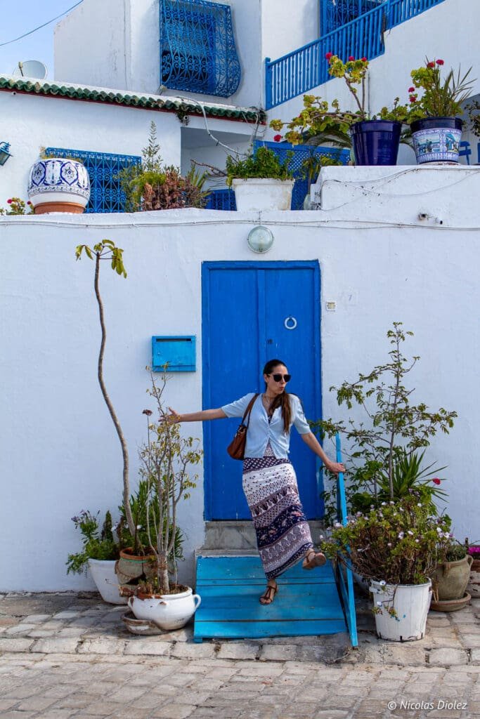 Femme posant devant porte bleue typique de Sidi Bou Saïd, Tunisie.