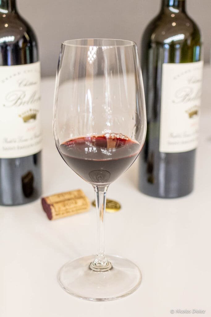 Glass of Château Angélus red wine with bottles and cork.