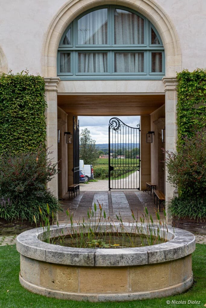 Entrance of a building, pond and view of the Château Angélus vineyard.