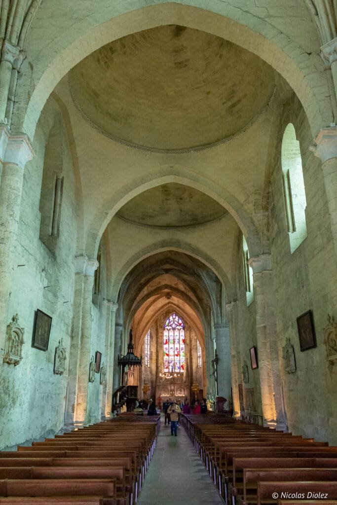 Interior of the monolithic church of Saint-Émilion with naves, stained glass and pews.