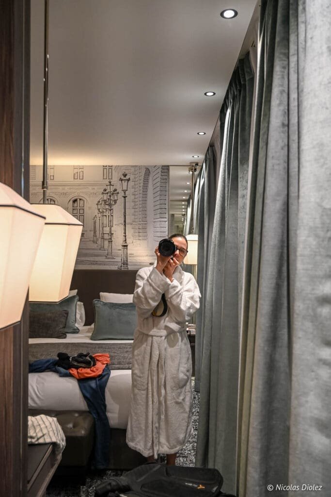 Femme en peignoir prenant une photo dans la chambre de l'Hôtel La Lanterne Paris.