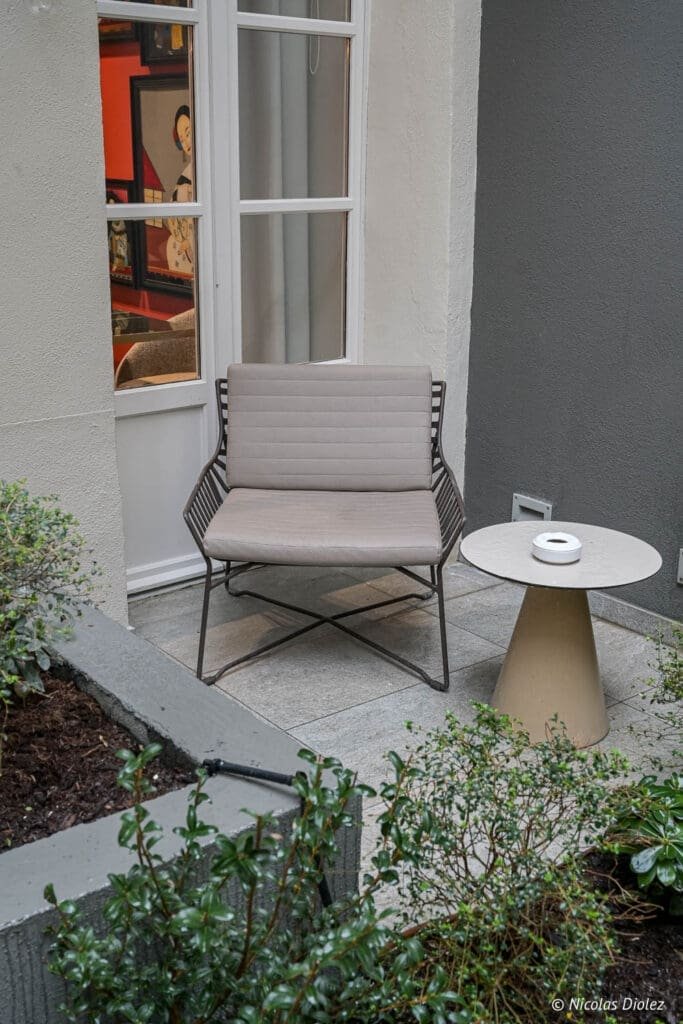 Fauteuil extérieur et petite table de jardin près de la porte vitrée de l'Hôtel La Lanterne.
