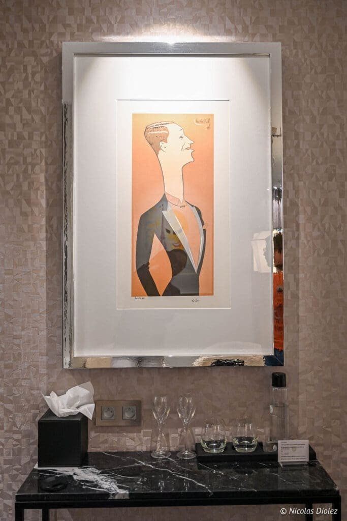 Caricature encadrée au-dessus d'un meuble en marbre avec verres et bouteille d'eau.