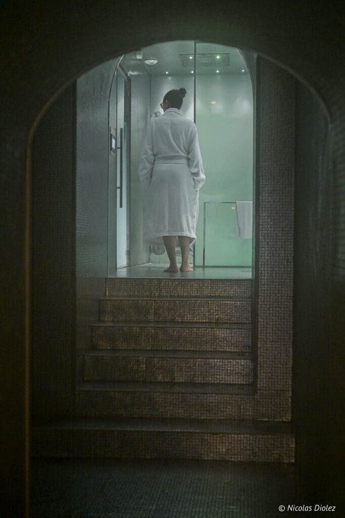 Femme en peignoir blanc montant des marches vers l'espace bien-être de l'Hôtel La Lanterne.