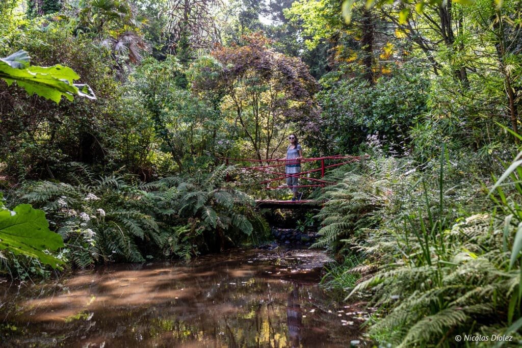Jardin en Hommage à Jacques Prévert, femme sur pont rouge au-dessus d'un ruisseau.
