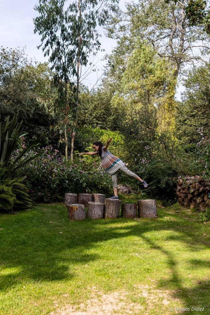 Femme en équilibre sur des rondins de bois dans le Jardin en Hommage à Jacques Prévert, Cotentin.