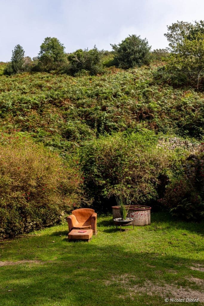 Jardin en hommage à Jacques Prévert Cotentin avec fauteuil orange et végétation luxuriante.