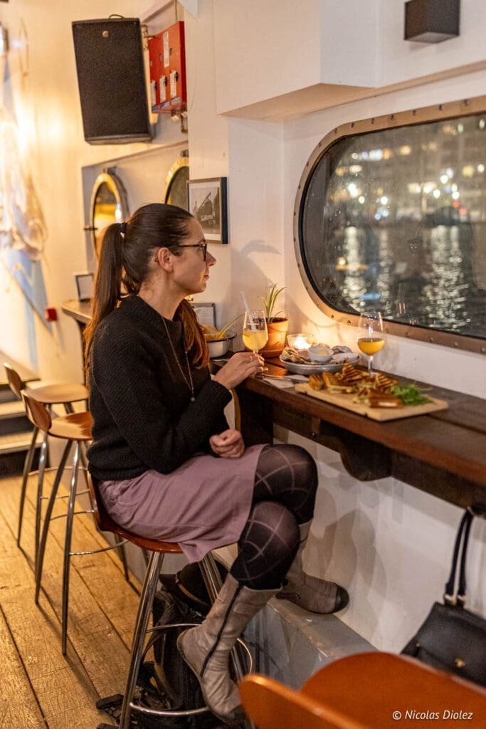 Femme buvant du vin et mangeant à La Bougeotte, bar à vin flottant à Paris.