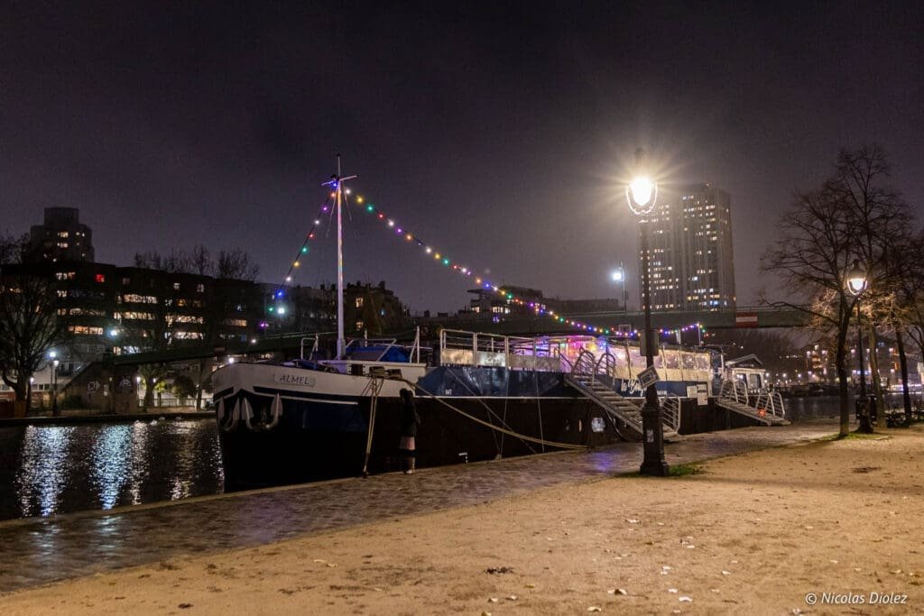 Péniche La Bougeotte, bar à vin flottant à Paris, illuminée la nuit.
