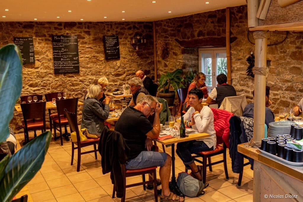 Intérieur restaurant La Malle aux Épices Cherbourg avec convives et menus sur mur en pierre.