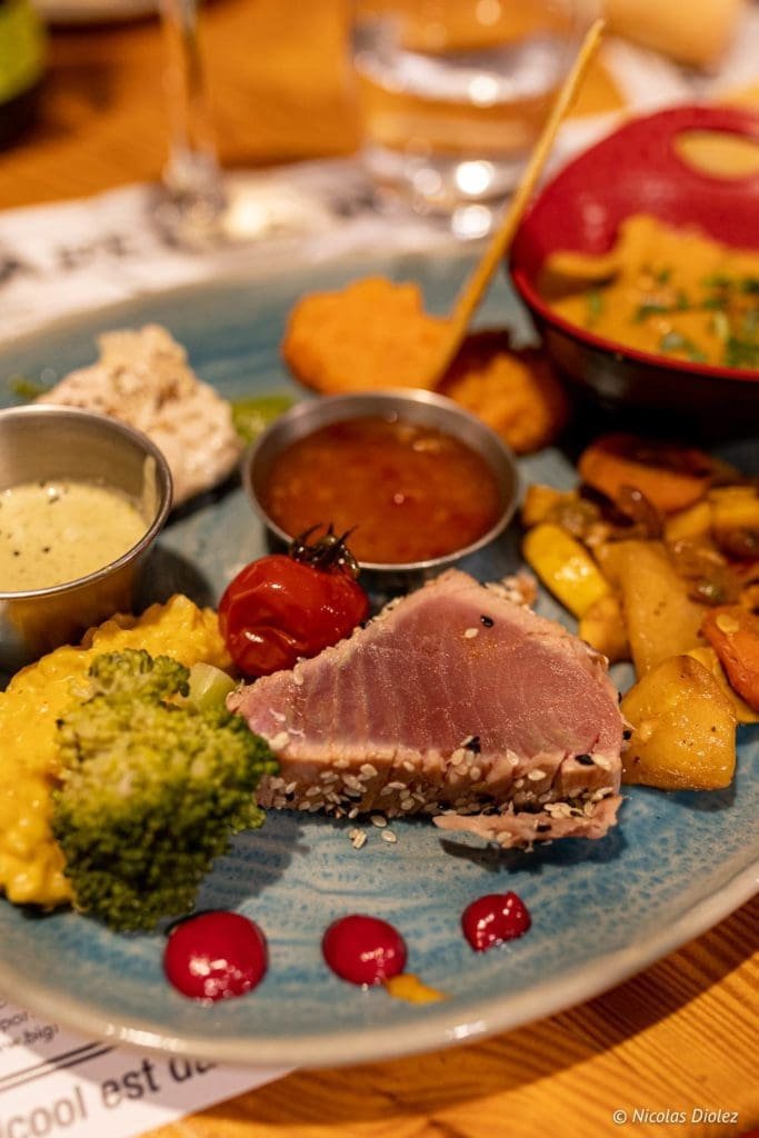 Thon mi-cuit sésame, légumes et sauces sur assiette bleue, La Malle aux Épices.
