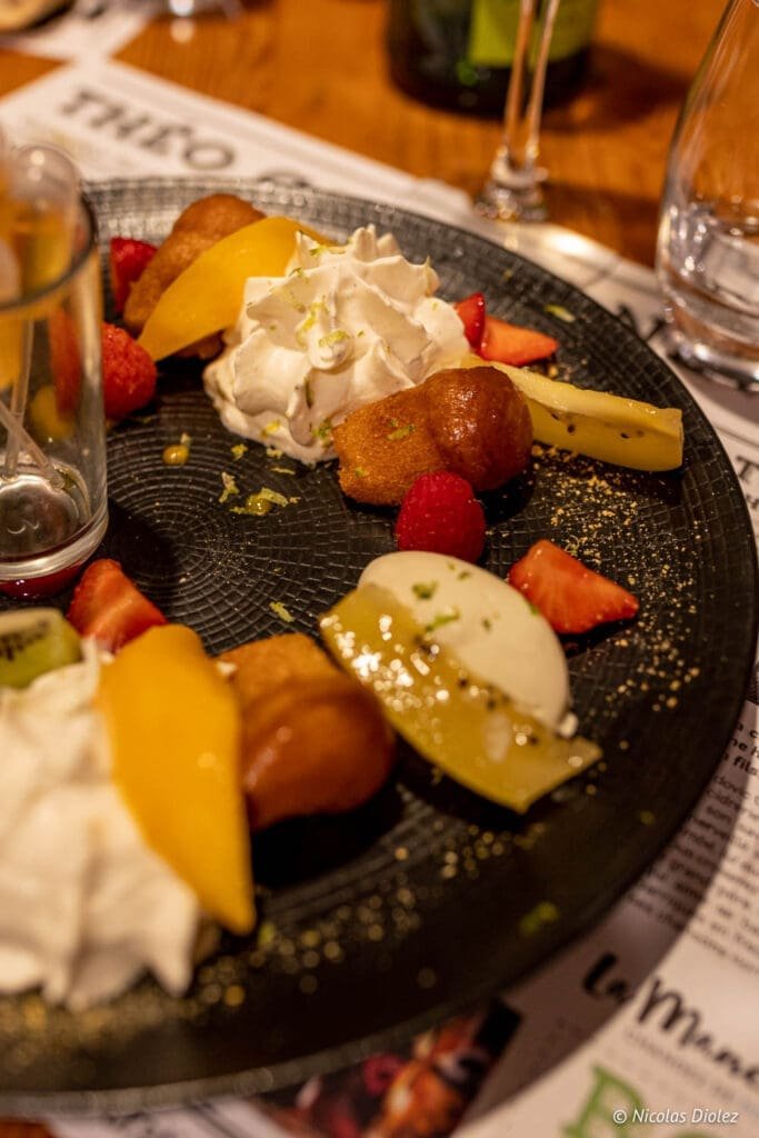 Dessert aux fruits, crème fouettée et baba au rhum sur assiette noire à La Malle aux Épices.