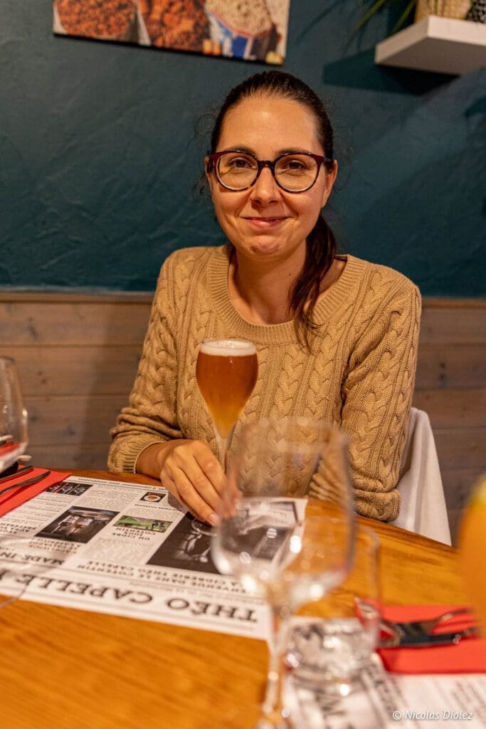 Femme souriante dégustant une bière à table, contexte Restaurant La Malle aux Épices.