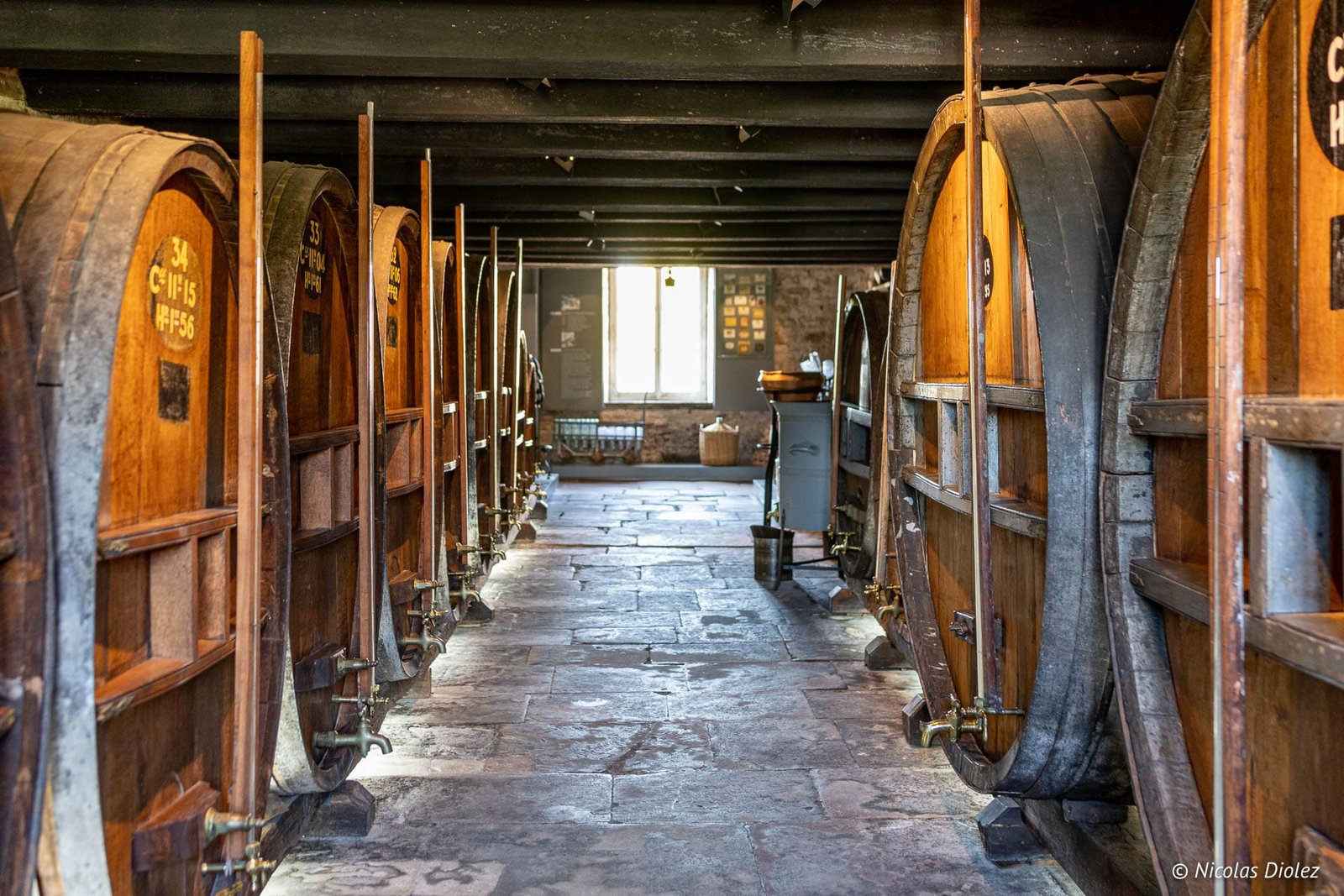 Intérieur cave avec grands foudres en bois étiquetés à l'Écomusée du Pays de la Cerise.