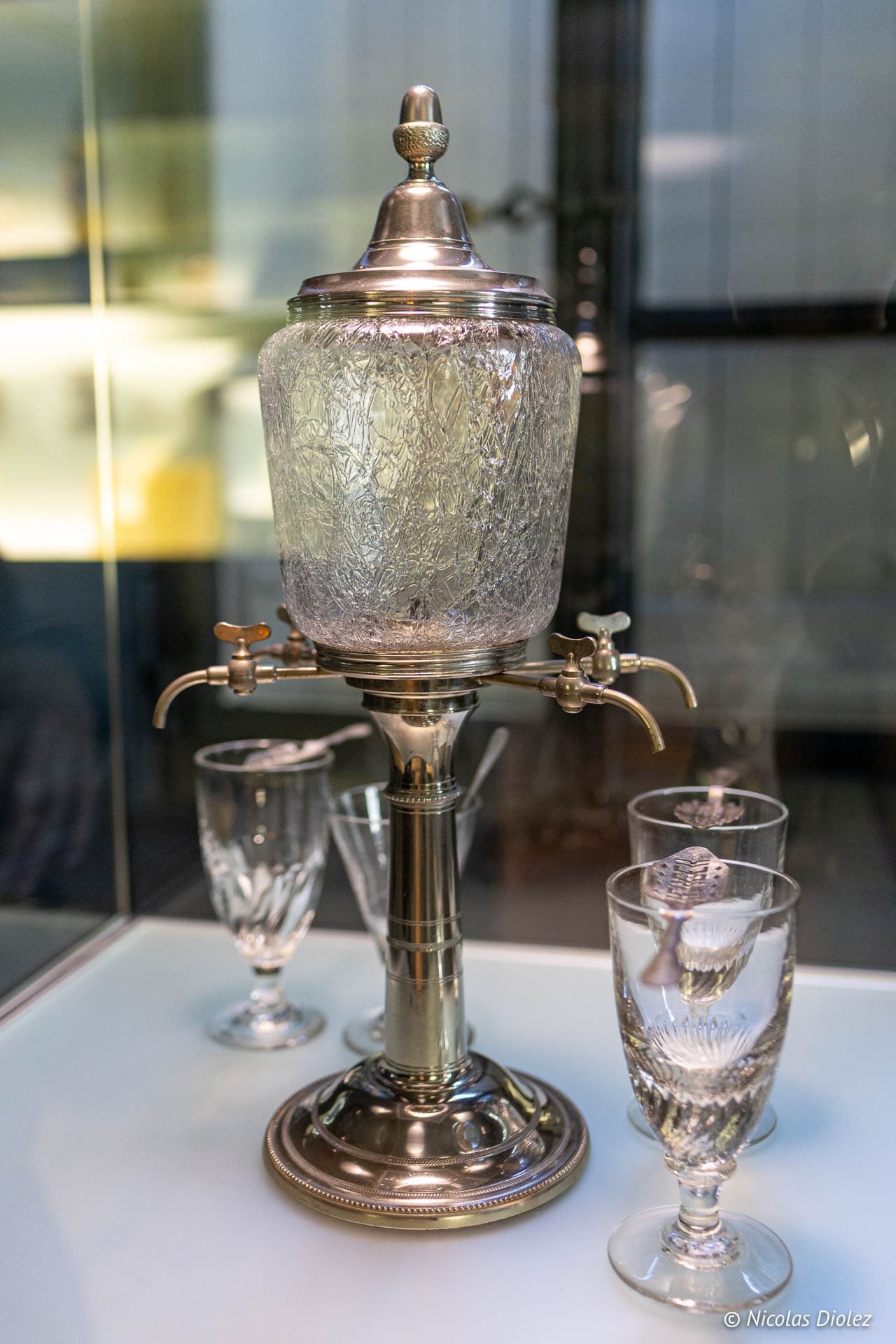 Absintheuse en verre et métal avec verres, exposition Écomusée Pays de la Cerise.