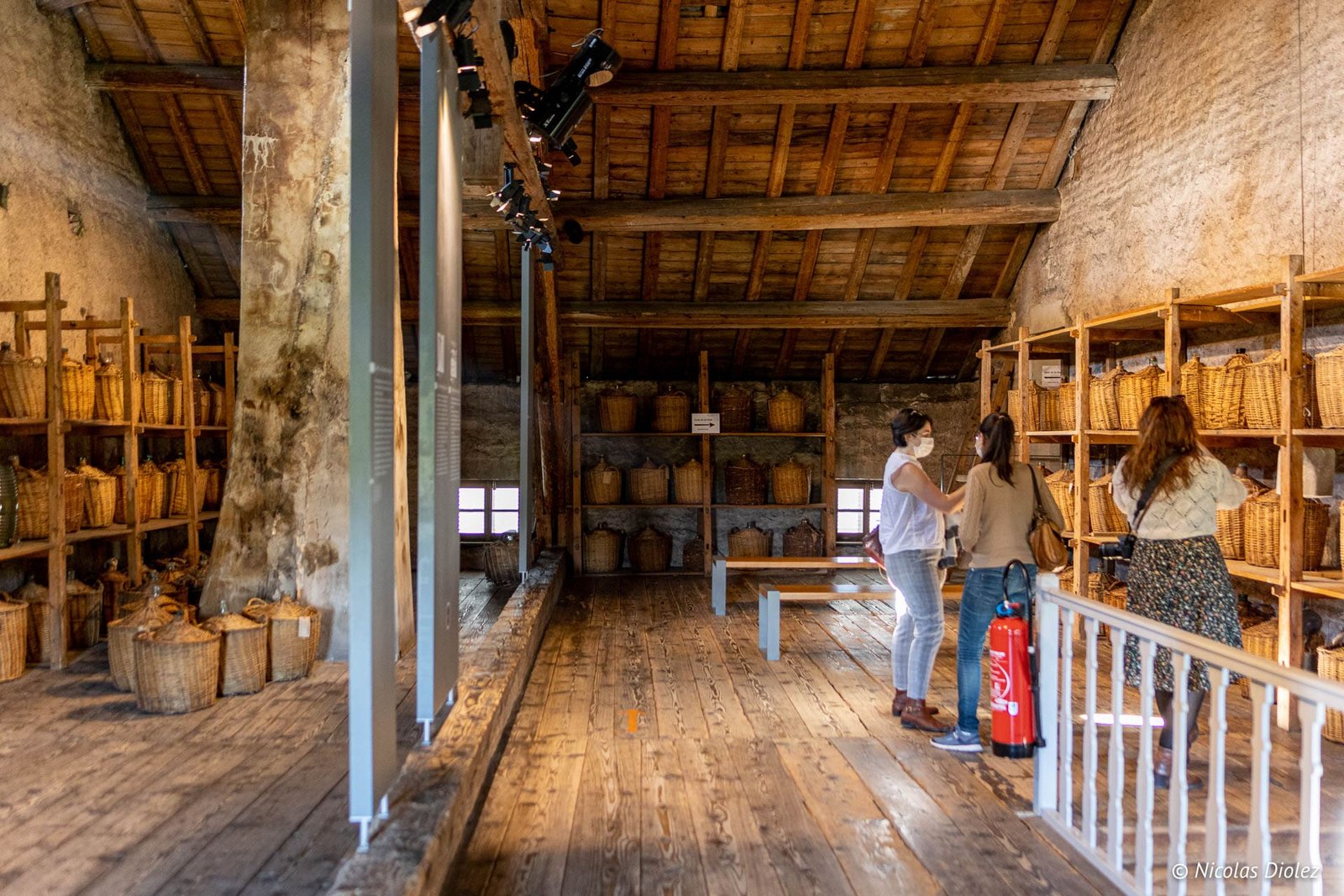 Intérieur de l'écomusée du Pays de la Cerise avec dames devant des bonbonnes de dame-jeanne.
