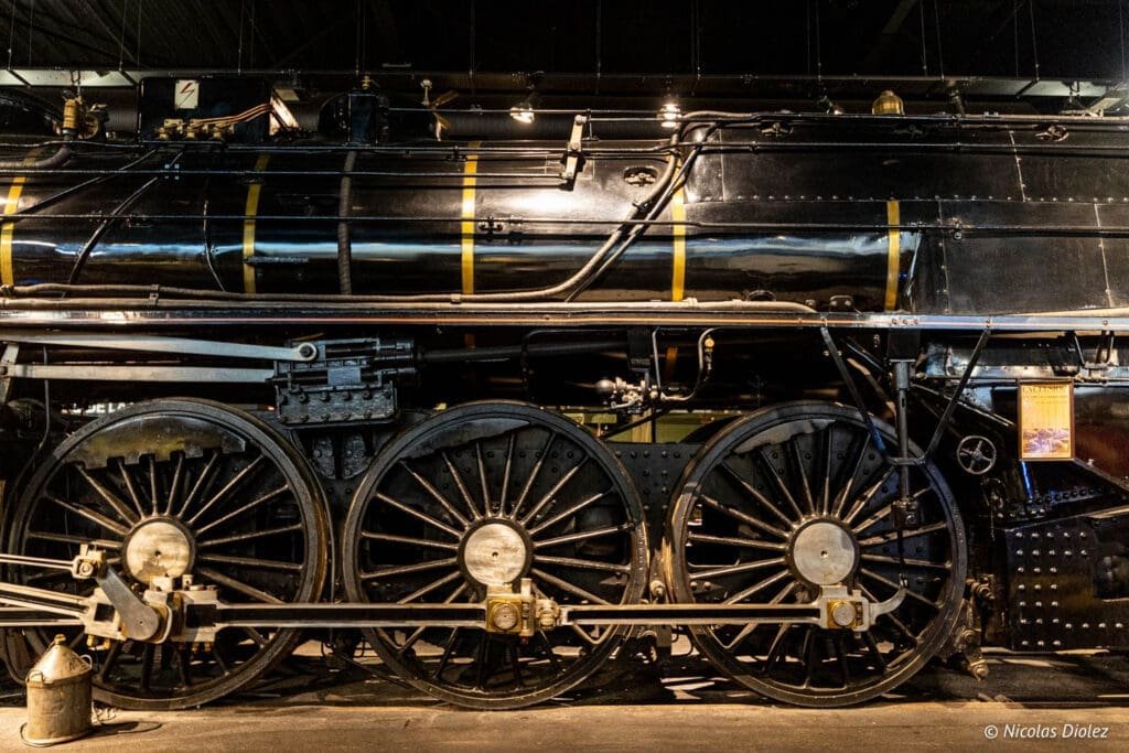 Gros plan sur les roues et la chaudière d'une locomotive noire à la Cité du Train Mulhouse.