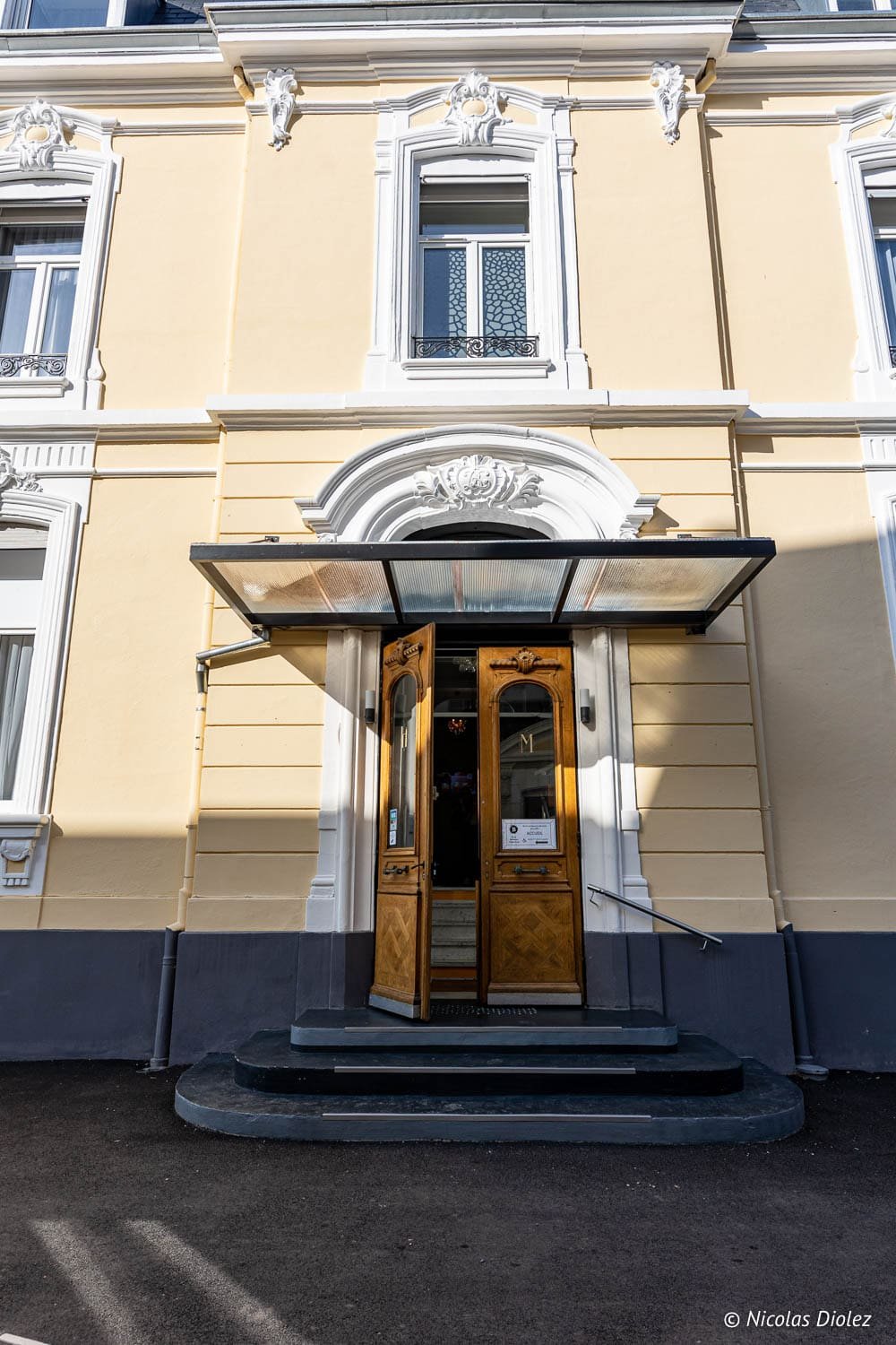 Façade et entrée de l'Hôtel Berti à Mulhouse avec porte en bois ouverte.