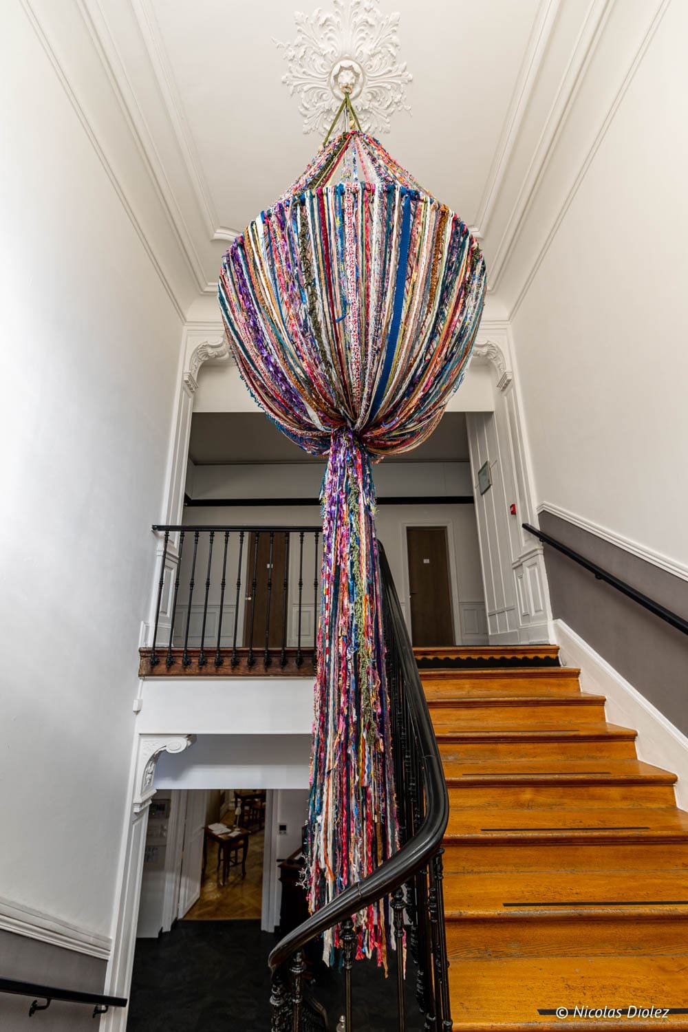 Suspension textile colorée au-dessus de l'escalier en bois de l'Hôtel Berti à Mulhouse.