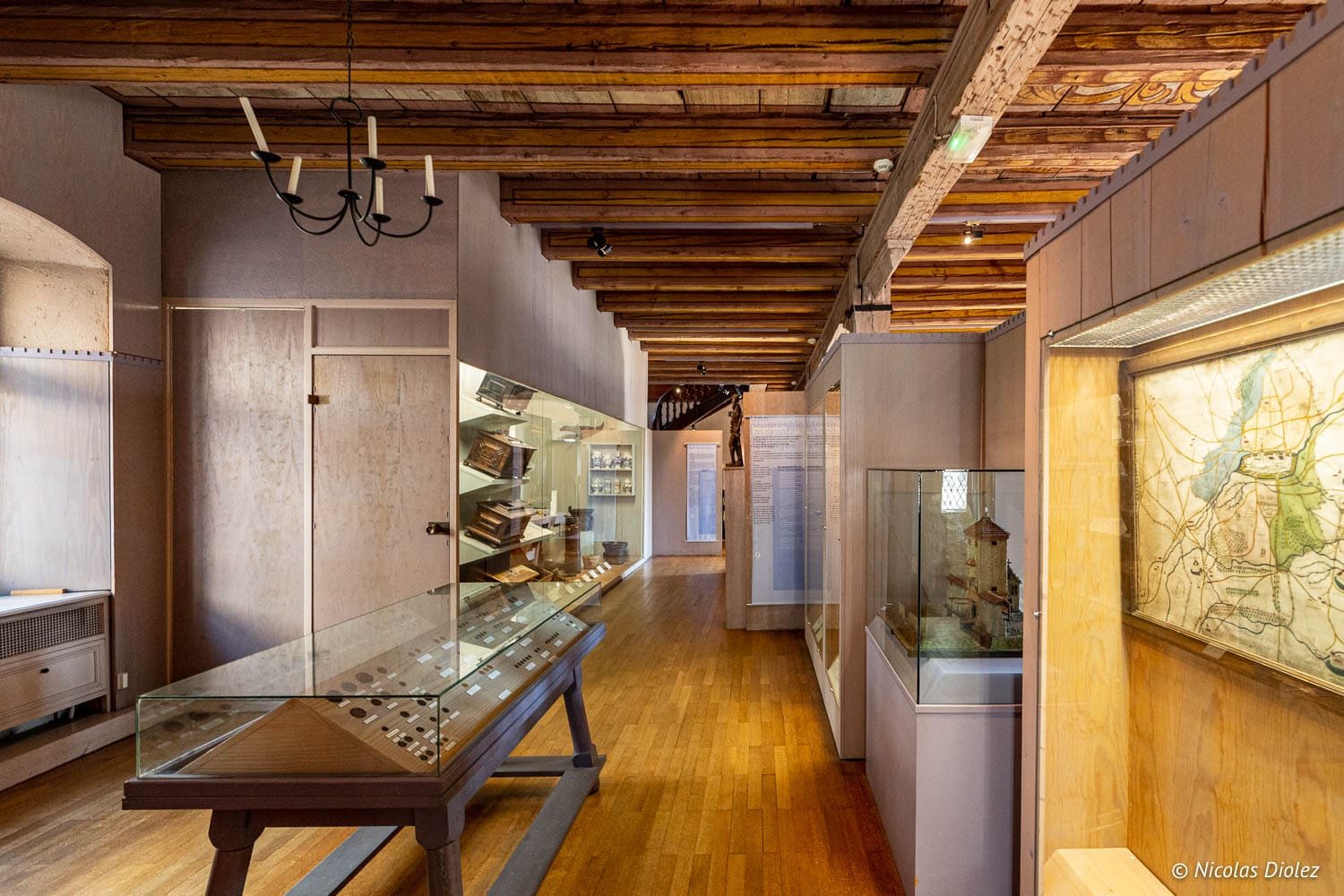 Intérieur du Musée Historique de Mulhouse avec poutres apparentes et vitrines d'exposition.