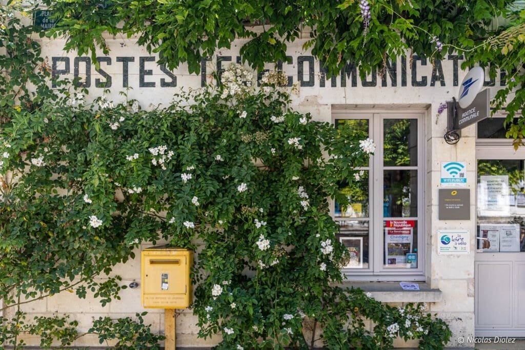 Old post office and yellow mailbox in Chédigny, near Loches, covered in roses.