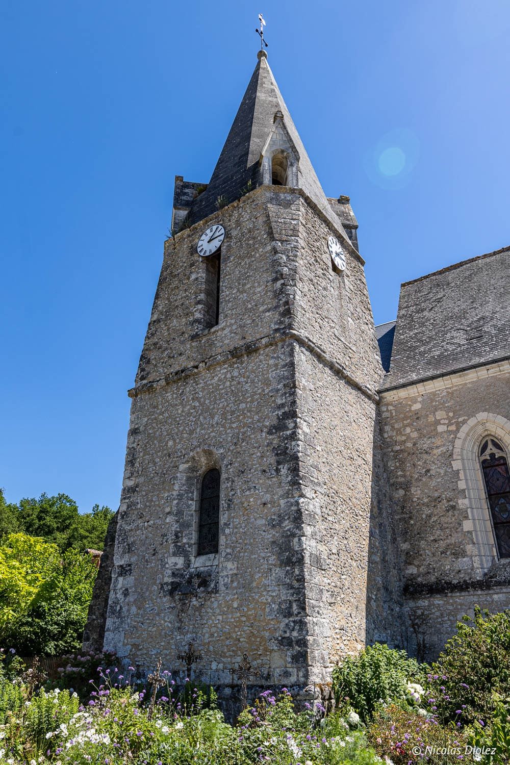 Clocher en pierre de l'église de Chédigny avec horloges et fleurs au premier plan.