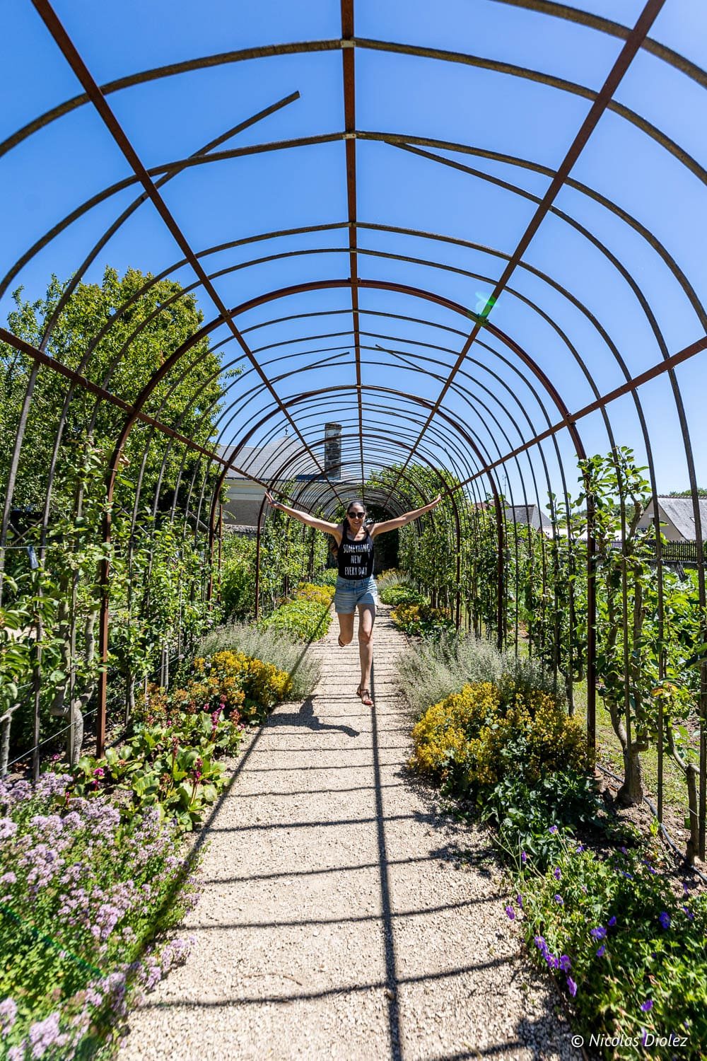 Femme courant sous une tonnelle fleurie aux jardins de Chédigny, Sud Touraine.