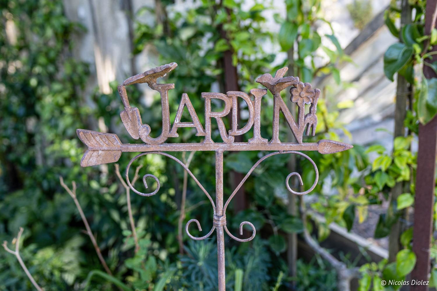 Enseigne rouillée avec inscription JARDIN et outils de jardinage sur fond verdoyant.
