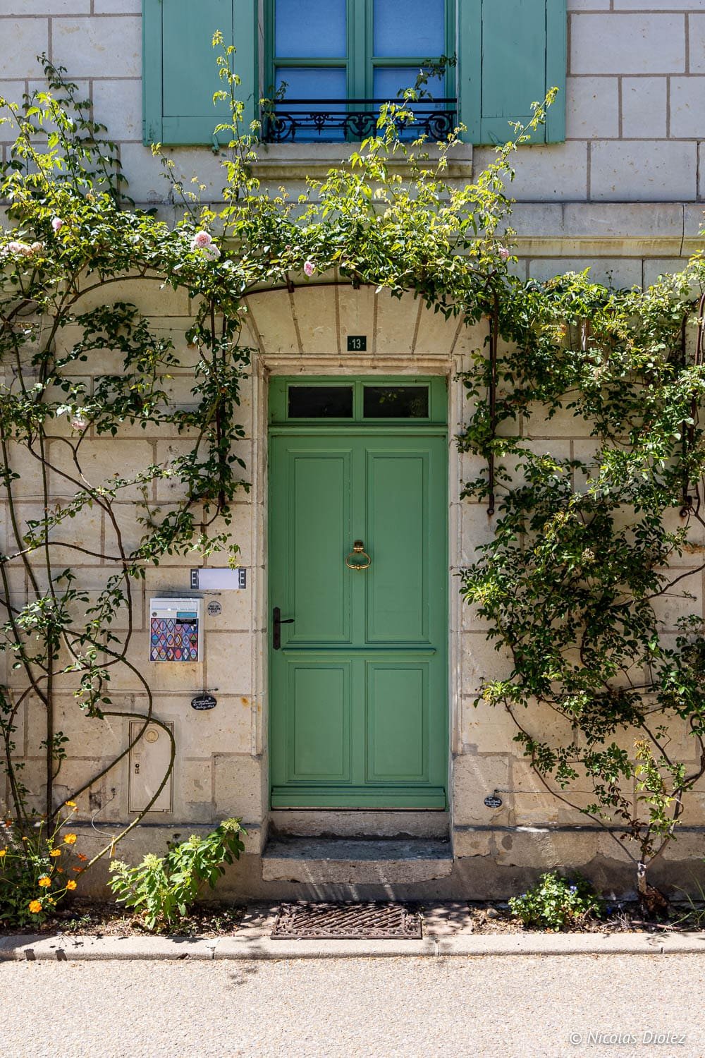 Porte verte au 13, façade en pierre blanche et rosiers grimpants à Chédigny.
