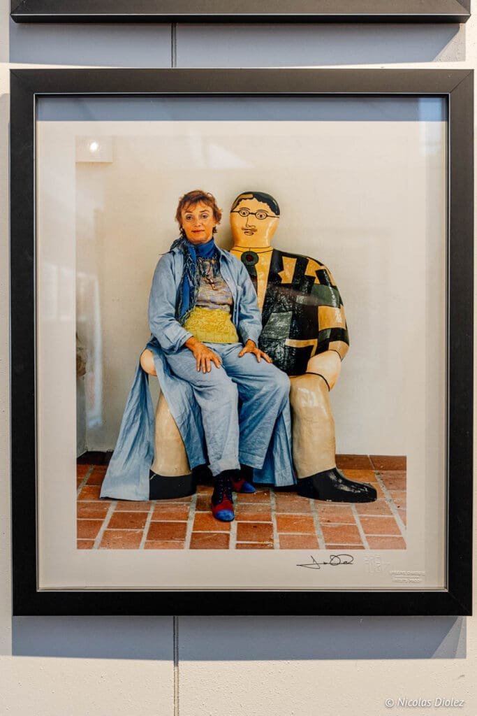 Exposition Jean-Marie Périer à Villeneuve d'Aveyron, femme assise près d'une sculpture.