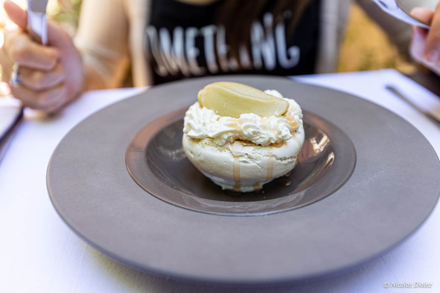Meringue dessert with cream and poached pear served on a grey plate.