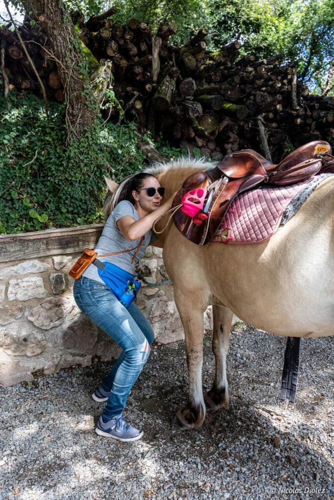 Femme préparant une selle sur un cheval lors d'une promenade dans les Bastides et Gorges de l'Aveyron.