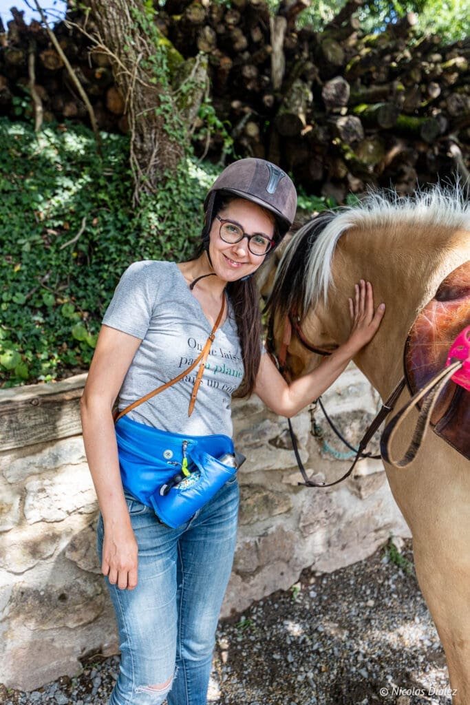 Promenade à cheval avec une femme souriante portant un casque et une sacoche bleue.