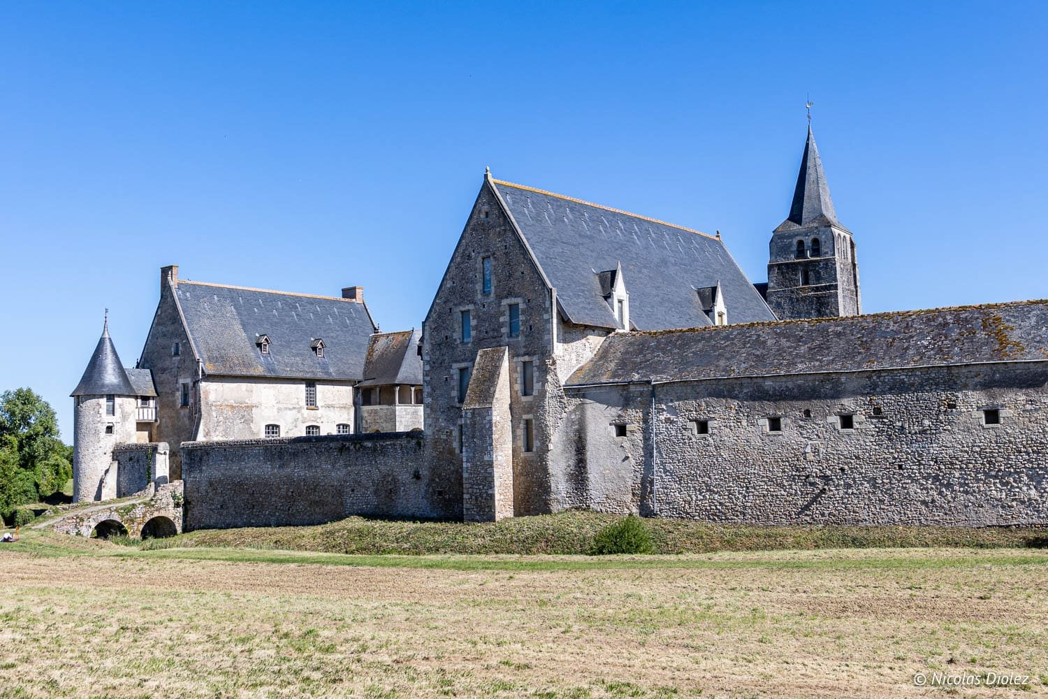 Enceinte médiévale de Loches avec sa tour et clocher sous un ciel bleu.