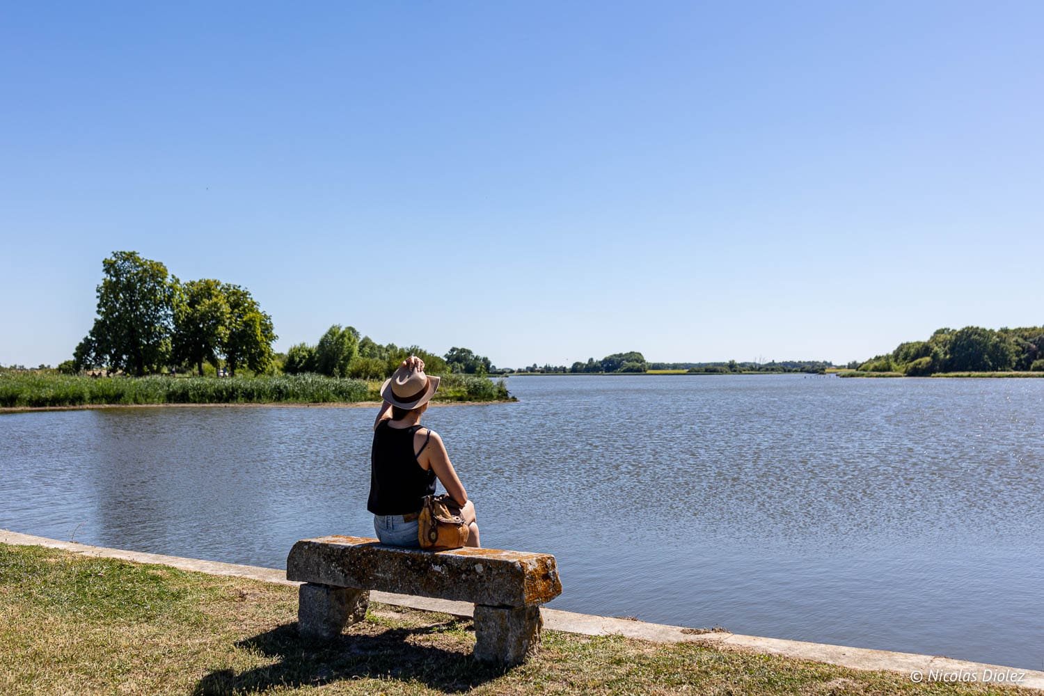 Randonnée au bord de l'eau près de Loches, femme assise sur banc pierre regardant lac.