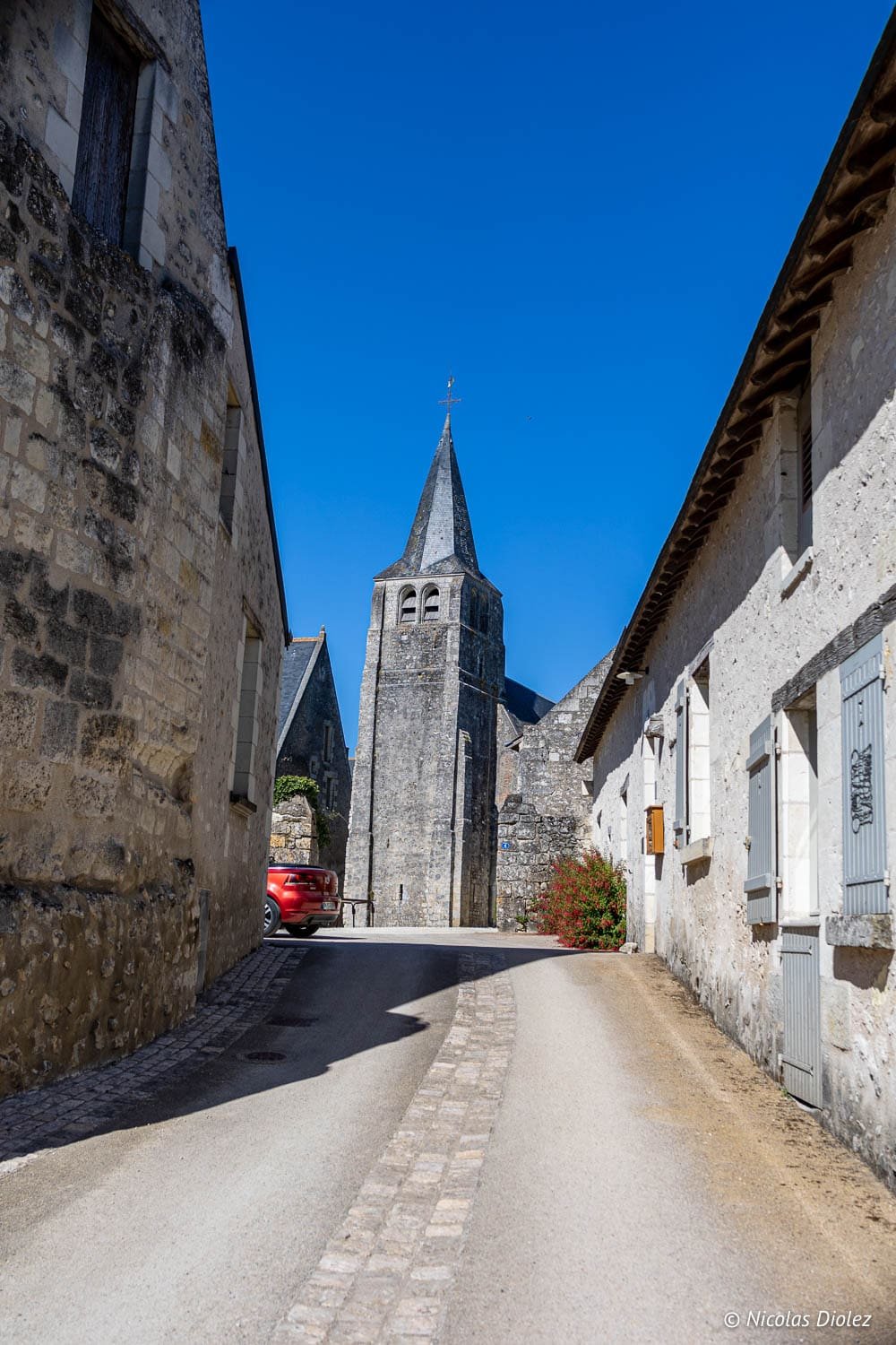 Rue de village ancienne menant à l'église de Loches sous un ciel bleu.