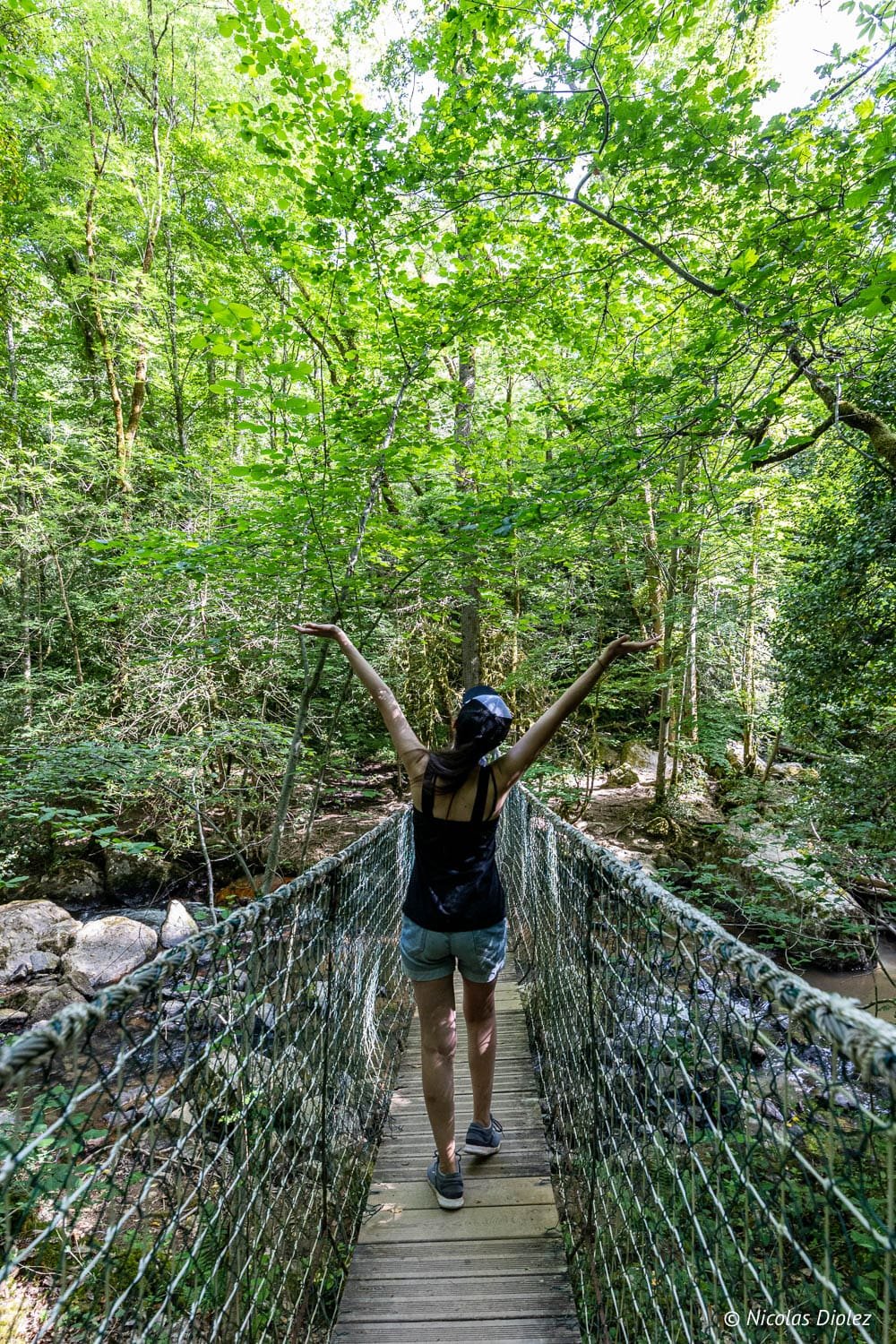Randonneuse sur pont suspendu en forêt près des Cascades d'Arifat.