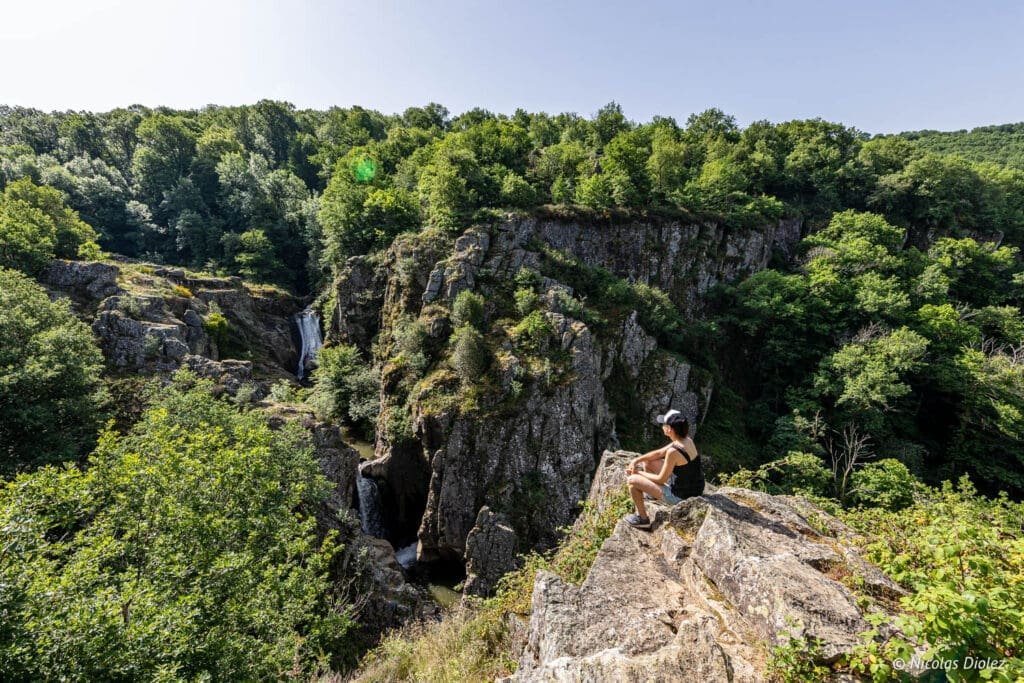 Randonneuse surplombant les cascades d'Arifat au milieu des falaises boisées.