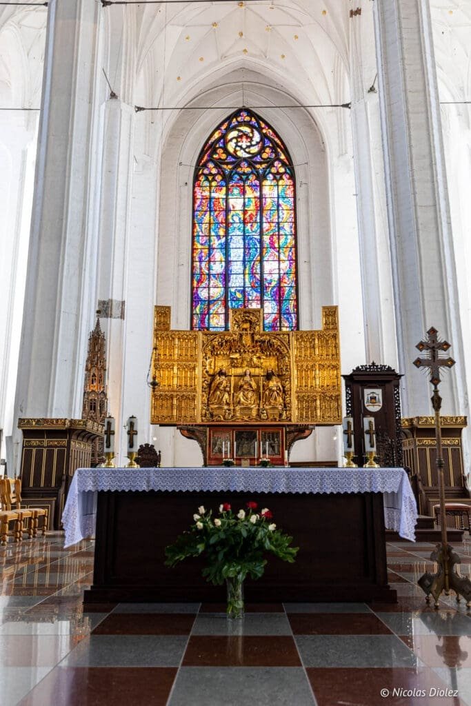 Intérieur Cathédrale de Gdańsk : autel doré, vitrail coloré, et sol à carreaux.