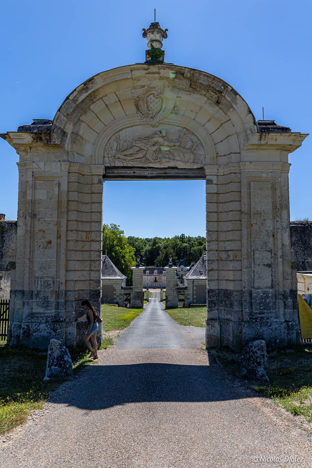 Portail sculpté menant à la Forêt de Loches et château en arrière-plan.
